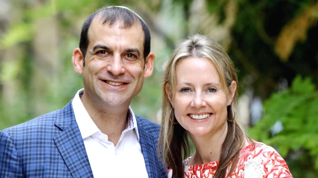 Two adults smiling for a photo outdoors with greenery in the background.