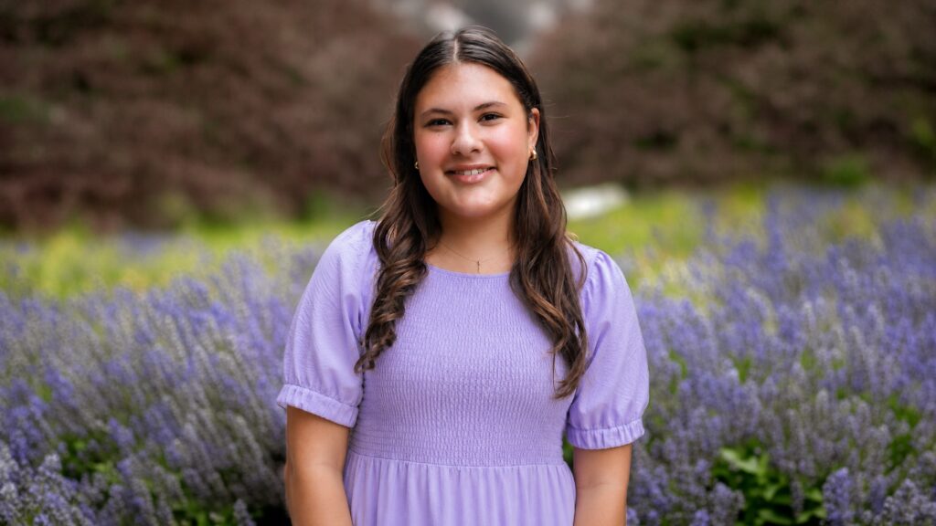 Smiling young woman in a lavender dress standing in a field of blooming lavender flowers outdoors.