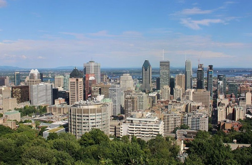 Wide view of a dense downtown skyline with tall office buildings against a blue sky, foreground filled with green trees and parkland.