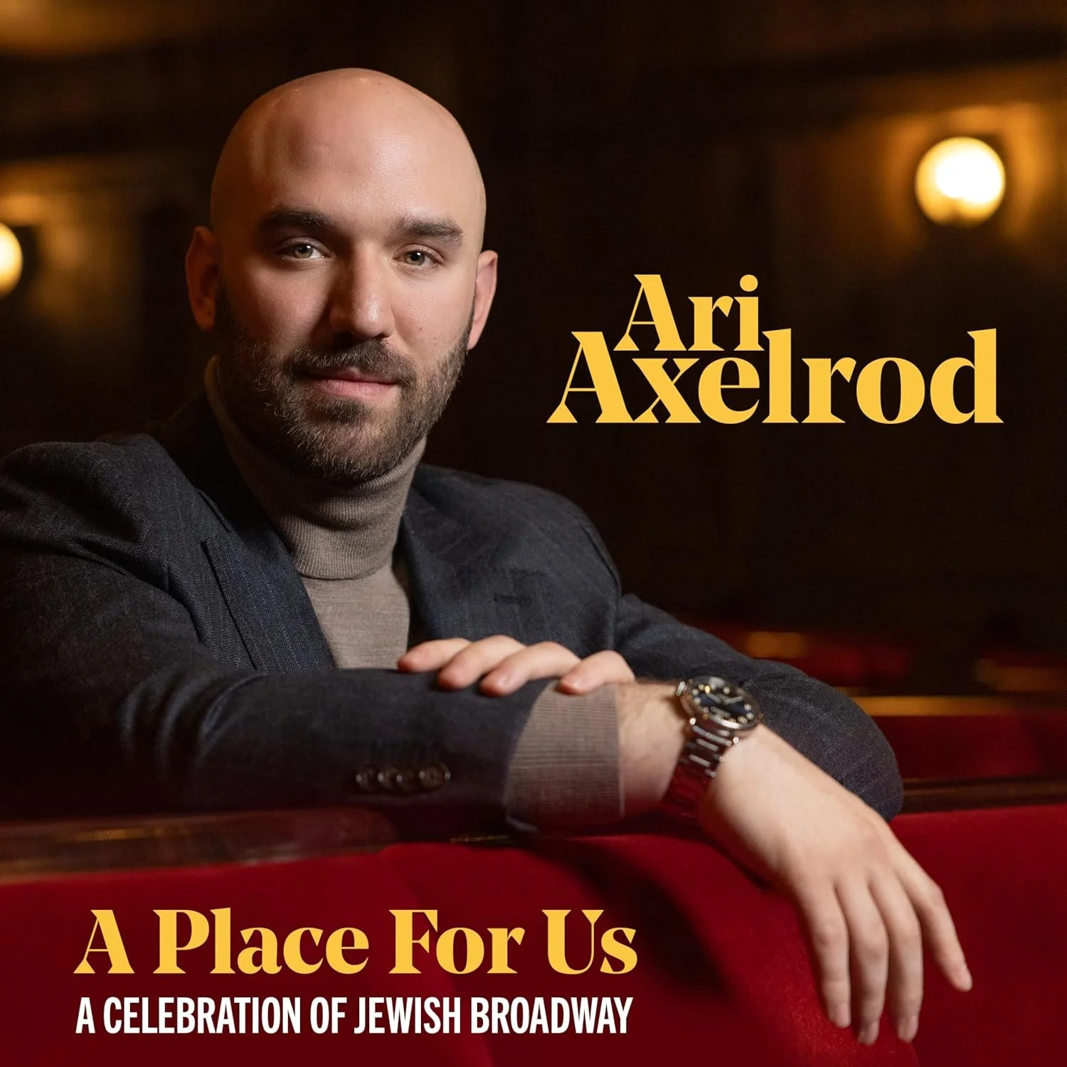Portrait of Ari Axelrod, a bald man with a beard in a dark blazer, leaning on a red velvet surface; text 'Ari Axelrod' and 'A Place For Us' appears on the right side.