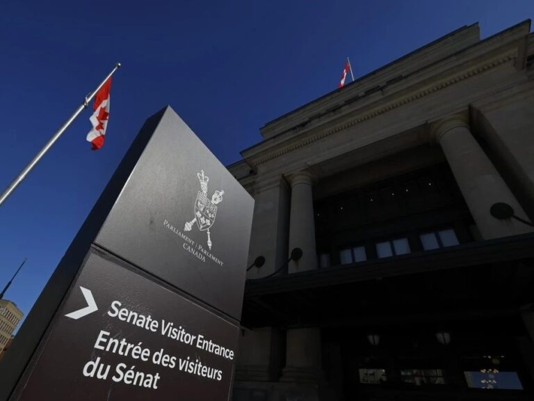 Sign directing to the Senate Visitor Entrance outside the Canadian Parliament building, with Canadian flags in the background.