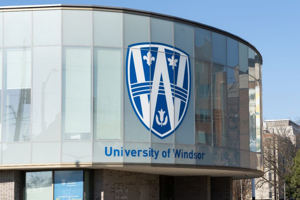 Curved glass facade of a university building with a large blue and white Windsor crest logo centered on the windows.