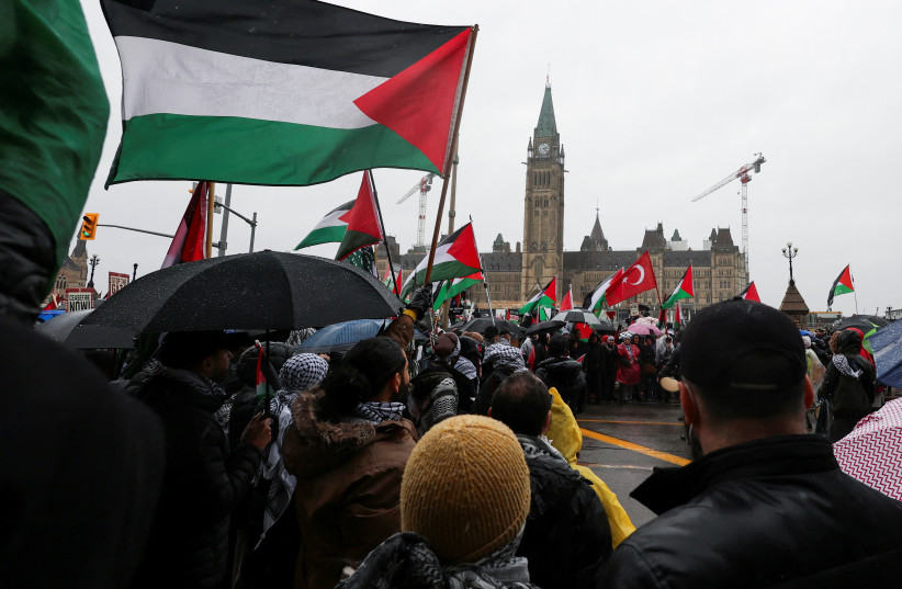 Crowd of protesters waving Palestinian flags on a rainy day in front of a historic government building with a clock tower in the background.