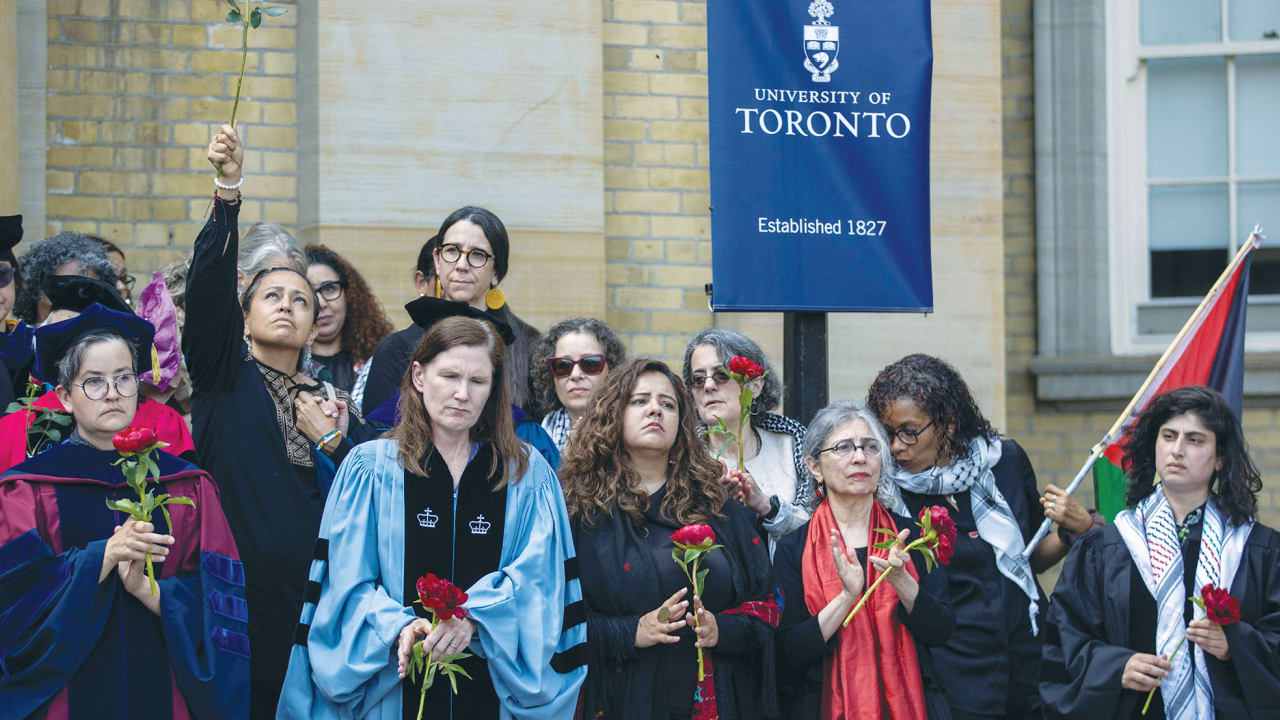 Group of graduates and faculty outdoors in academic robes, some holding red roses, with a University of Toronto banner in the background.