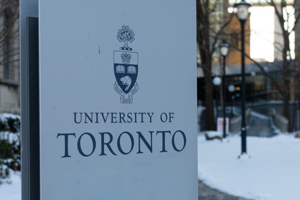 Sign for the University of Toronto with its crest and motto in blue, outdoor snowy scene in the background