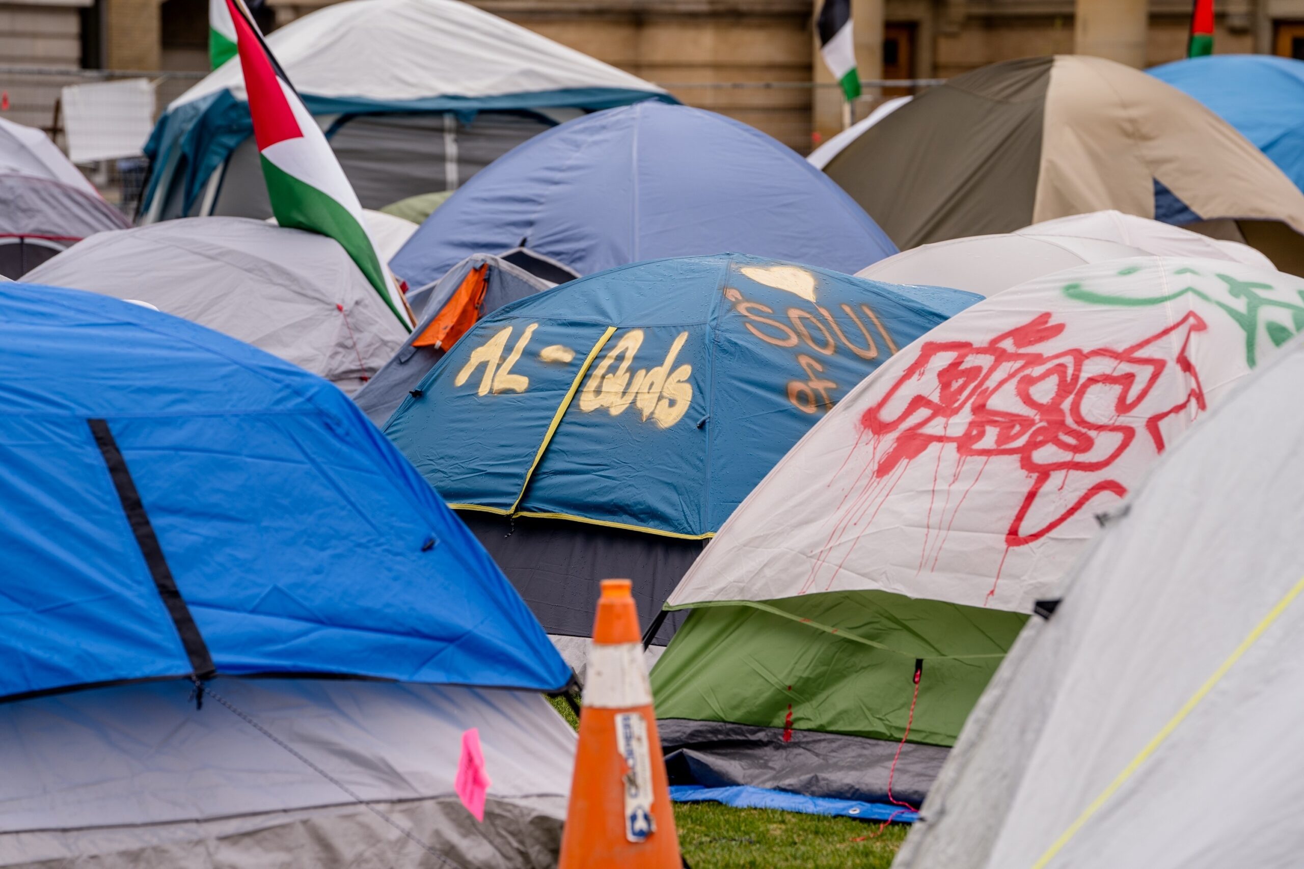 Rows of colorful tents pitched together in a street protest camp, with an orange traffic cone in the foreground.