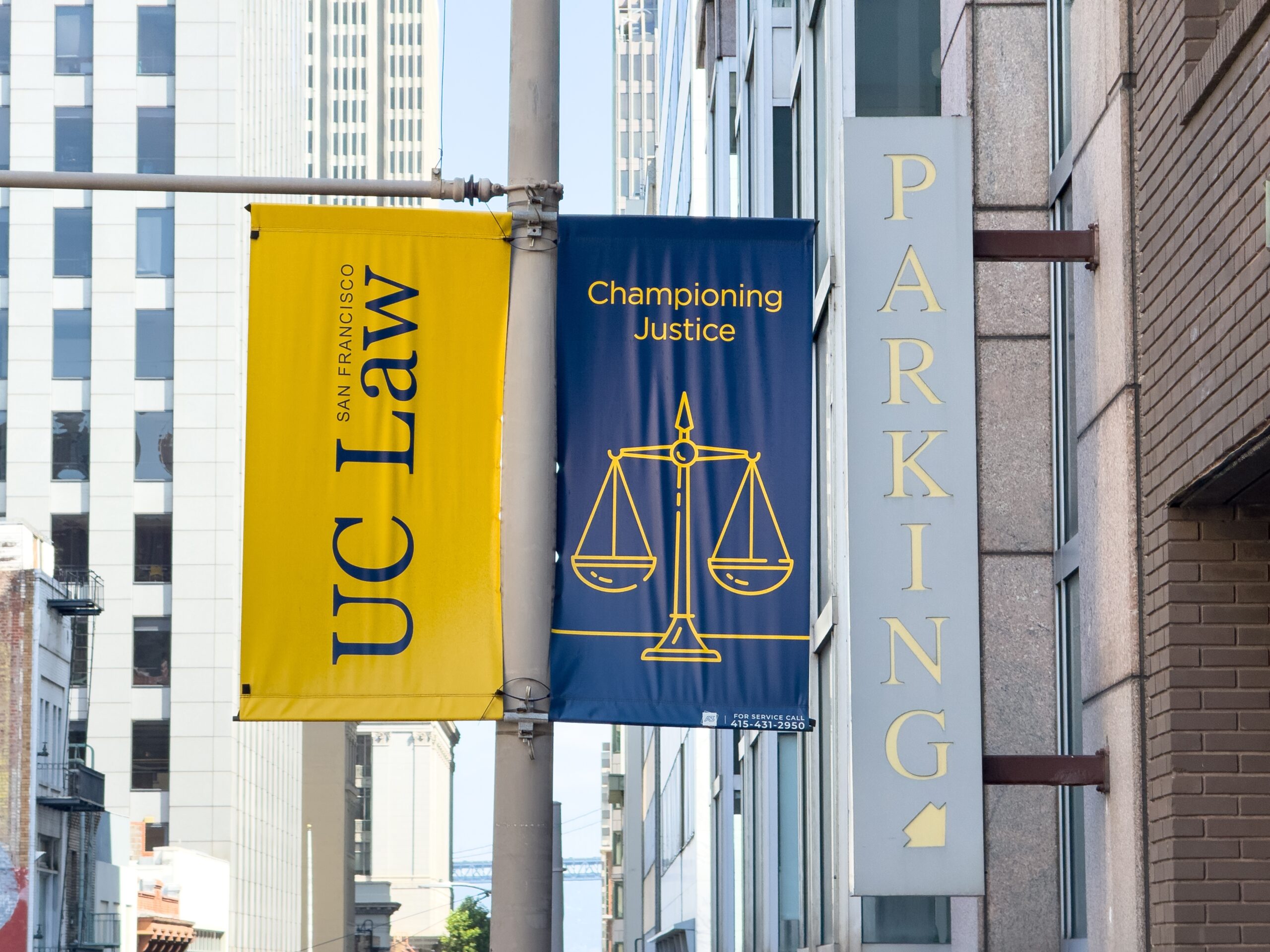 Blue banner reads 'Championing Justice' with a scales-of-justice icon; yellow banner for a law firm beside it; vertical 'PARKING' sign on the building.