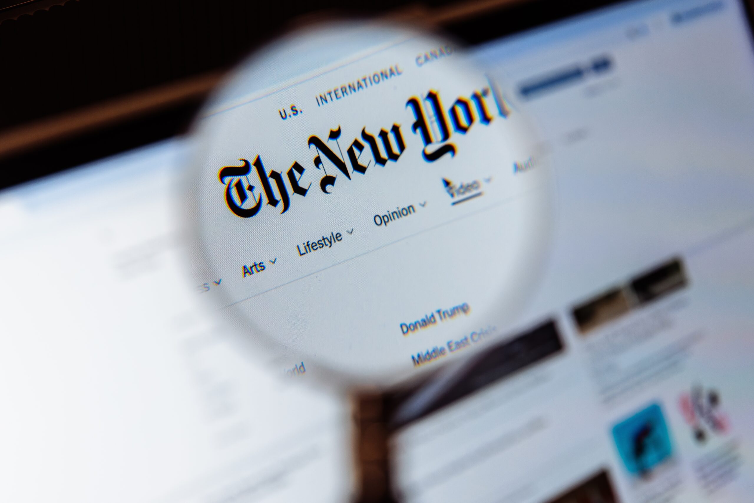 Close-up of a computer screen showing The New York Times homepage with navigation links visible at the top and article sections below.