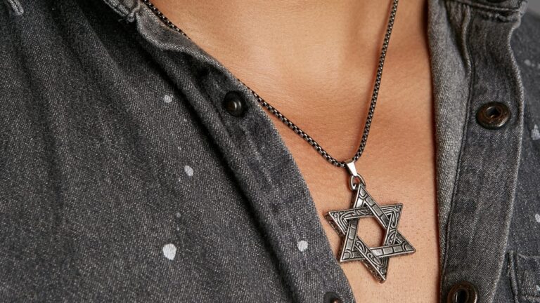 Close-up of a silver Star of David pendant on a black chain resting on a dark denim shirt