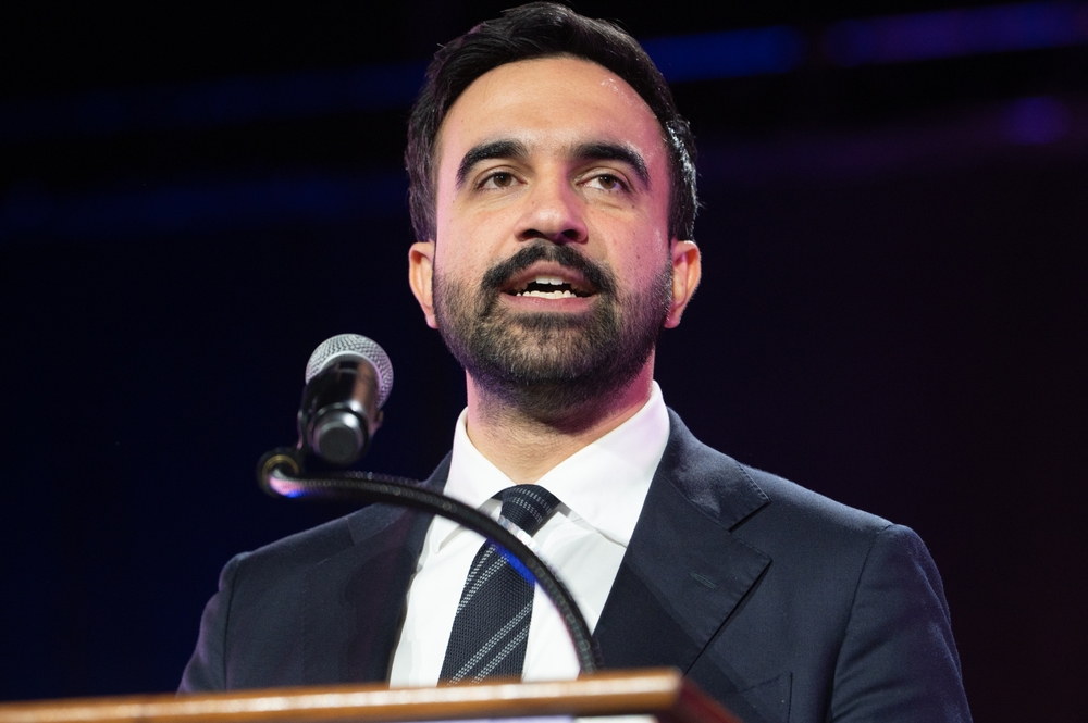 Man in a dark suit and tie speaks at a podium with a microphone during a formal event.