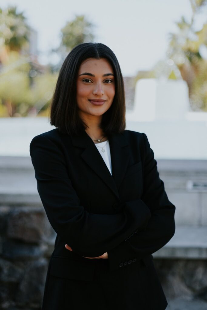 Professional woman with shoulder-length black hair in a black blazer, standing outdoors with arms crossed.