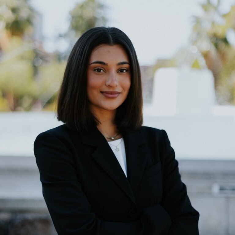 Professional woman with shoulder-length black hair in a black blazer, standing outdoors with arms crossed.