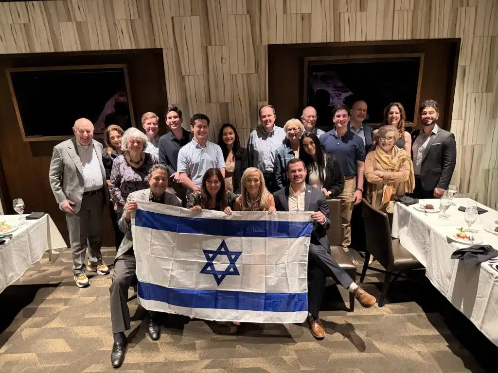 Group of people posing with an Israeli flag in a restaurant dining room during a social gathering.