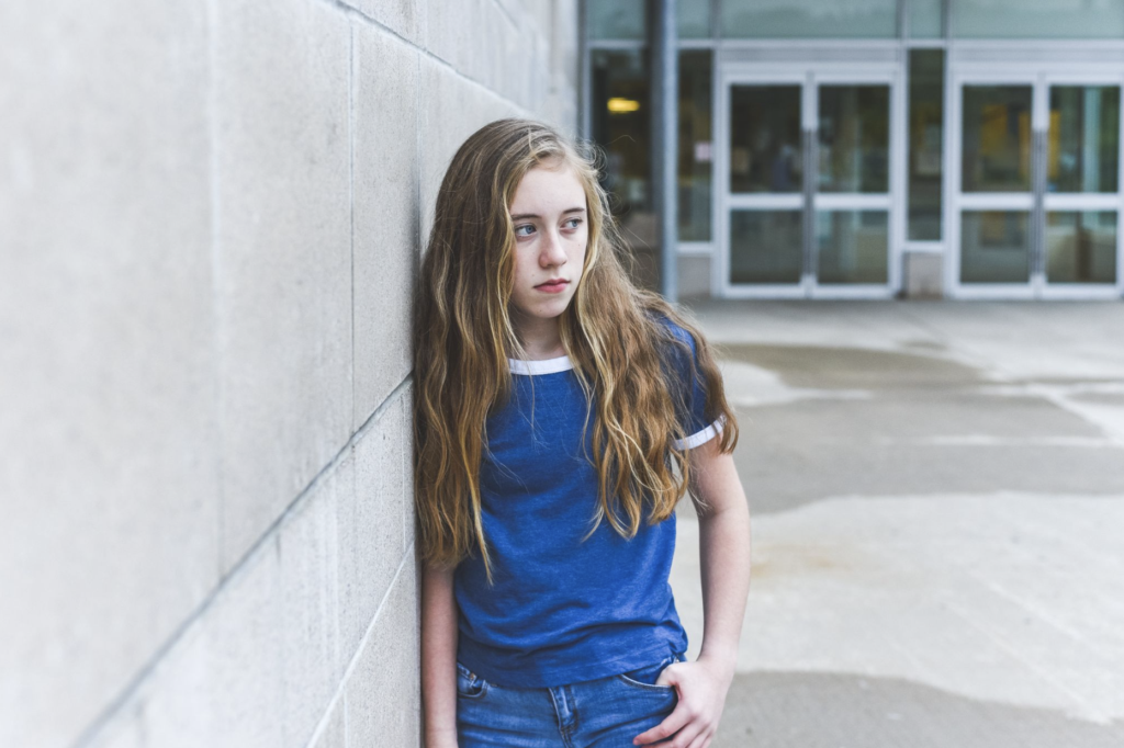 Sad high school student standing alone on campus.