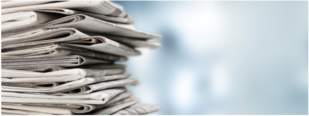 Stack of folded newspapers piled on a desk against a light blue background while ready for distribution.