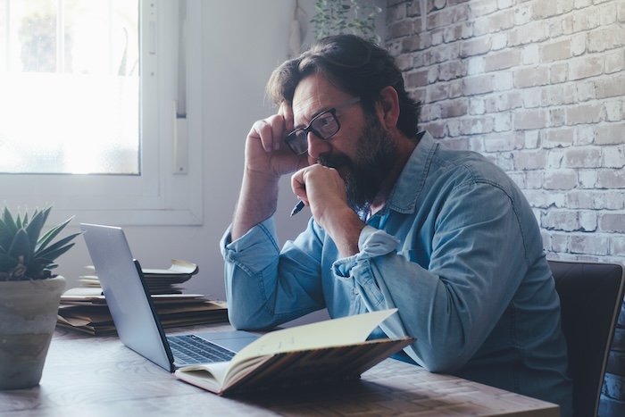 Concerned middle-aged man taking notes and submitting a report online.